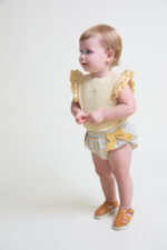 Camiseta sin mangas en color amarillo con detalle de volantes en los hombros y cierre trasero y braguita a juego con estampado de cuadros en tonos amarillo y celeste, decorada con lazos laterales y cintura elástica. - Imagen 2