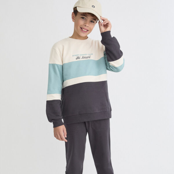 Sudadera en bloques de color crudo, azul verdoso y gris oscuro con detalle bordado “Ski Resort”. Pantalón a juego con cintura elástica y puños ajustados.
