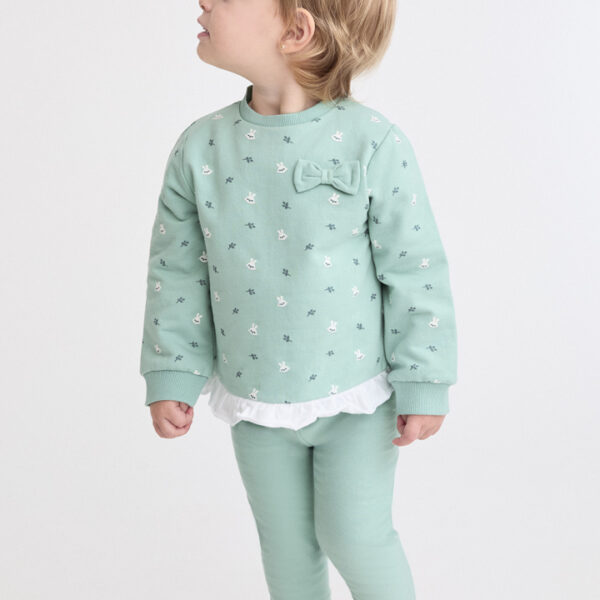 Sudadera verde con estampado de conejitos, volantes blancos en el bajo y lazo decorativo en el pecho. Leggings lisos a juego.