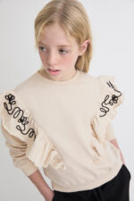 Conjunto con sudadera beige de felpa suave con volantes y bordado decorativo en hombros. Pantalón negro de punto elástico, cálido y confortable. - Imagen 2